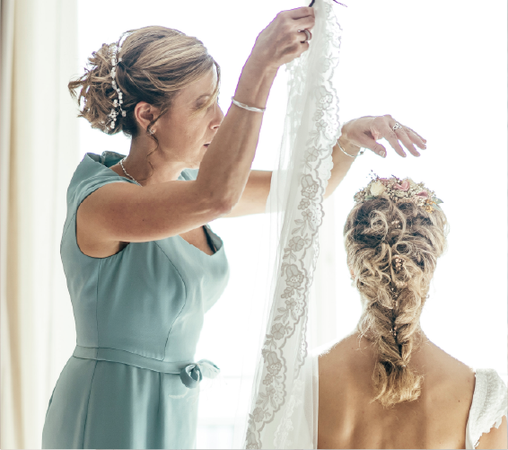 Bridesmaid helping bride with wedding dress in front of window