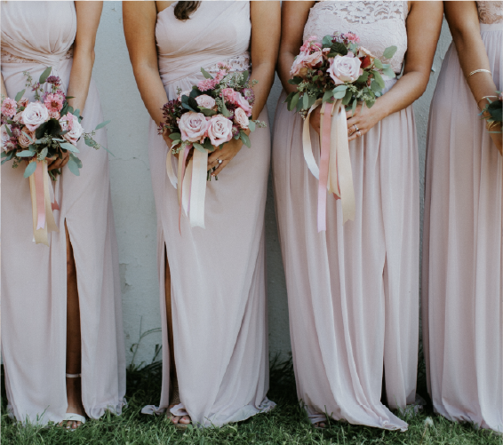 Bridesmaids in pink dresses holding bouquets of flowers in front of a wall