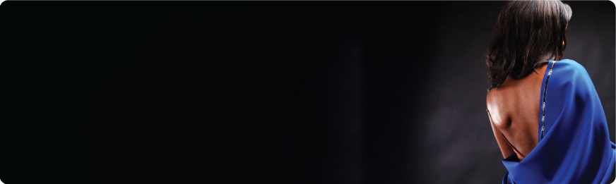 A black woman with dark hair is seen from the back draped in blue fabric on a black background