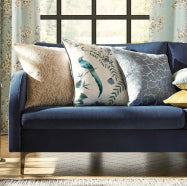 A blue couch with three decorative patterned pillows in front of a window with light blue curtains