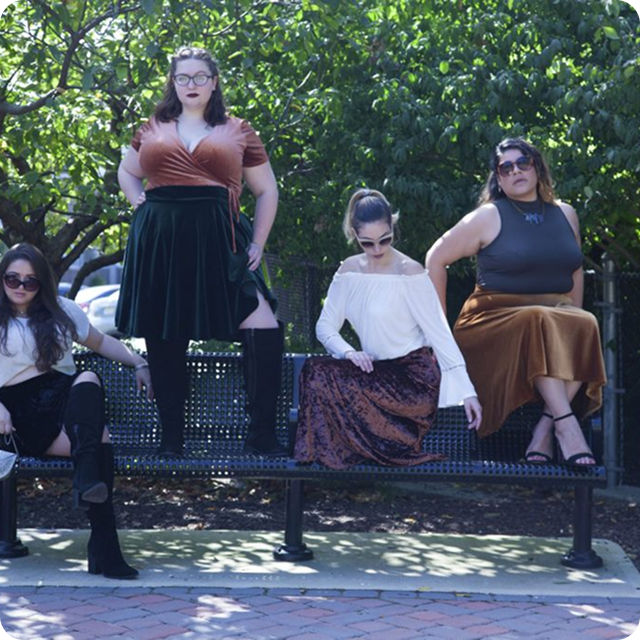 Several women sitting on a bench in a park with trees