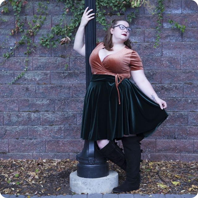 Woman in a dress and boots leaning against a pole