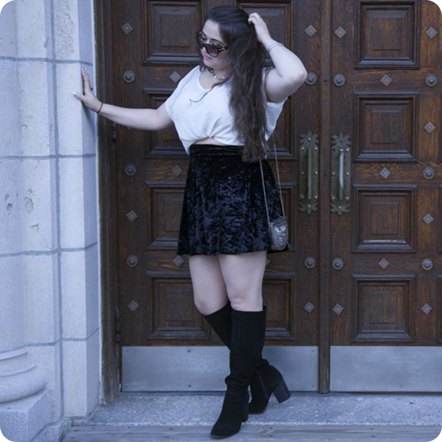 Woman in a black skirt and white shirt leaning against a door