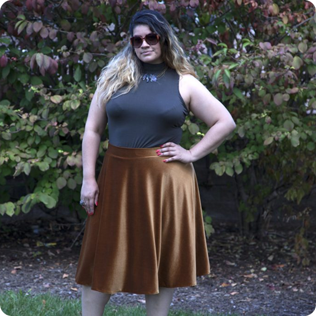 Woman in a skirt and sunglasses standing in front of a bush
