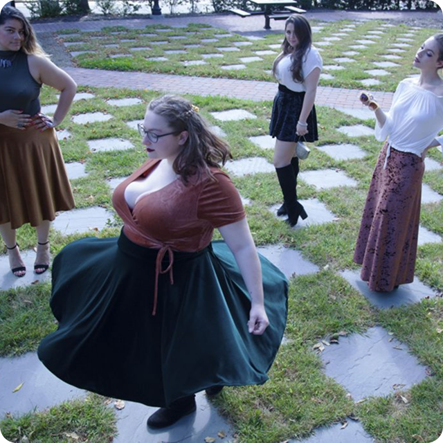 Several women in dresses are standing in a circle on a stone path