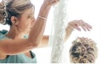 Bride putting on wedding dress in front of window with veil